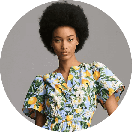 صورة امرأة ذات شعر مجعد ترتدي فستان مزهر ملون، تعبر عن الأناقة والجمال الطبيعي.